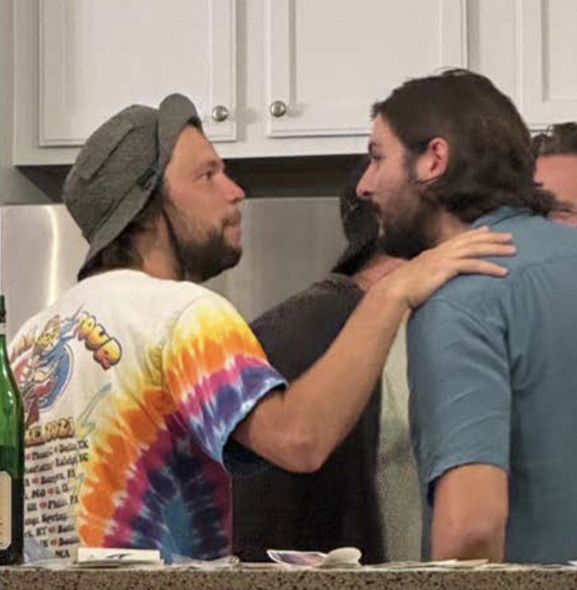 Two men in tense conversation apart from the group, one holding a note up between them.