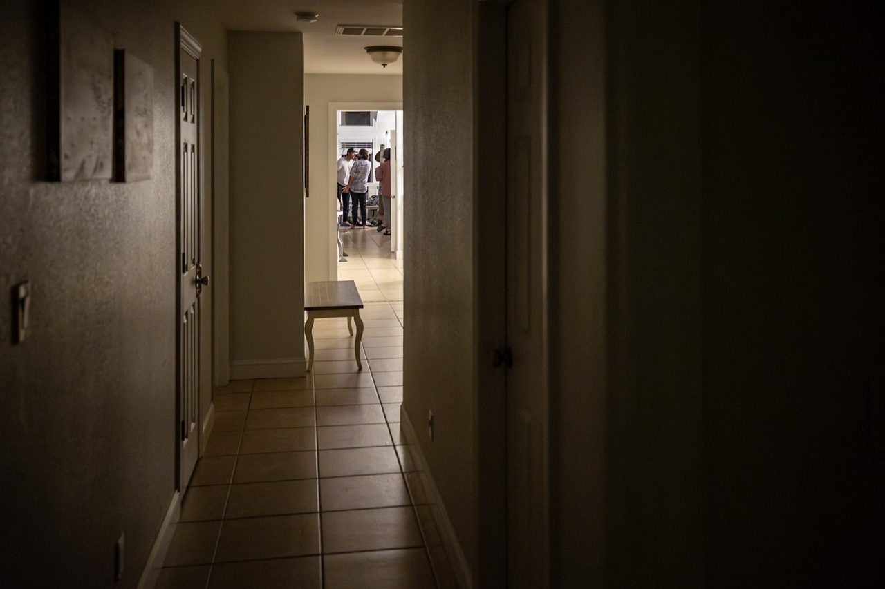 A hallway outside a closed door where karaoke equipment sits idle while men confer in the next room.