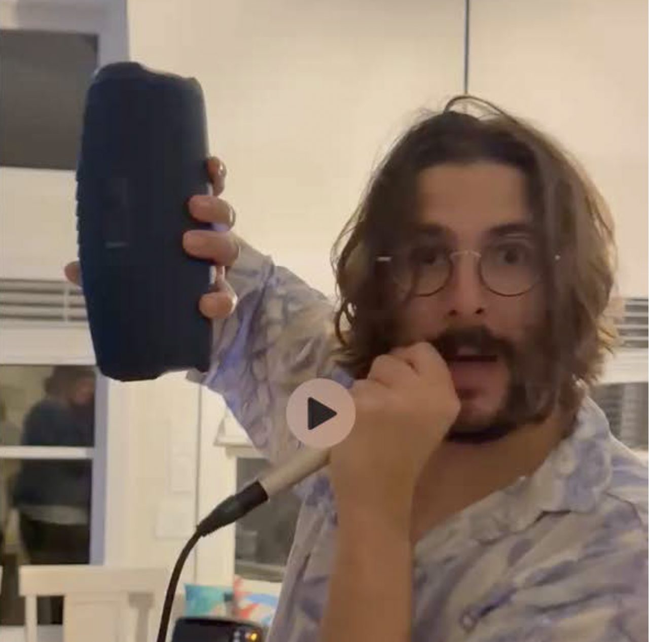 A man sings into a microphone under colored party lighting in the living room.