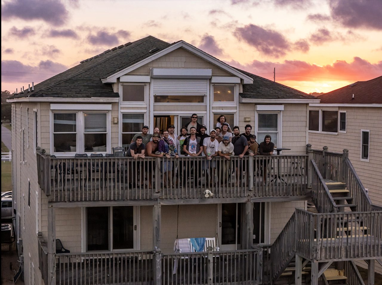 An aerial drone photograph of the whole group waving from the third-story deck of the beach house.