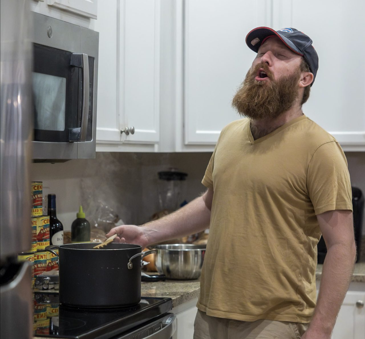 A man stirs a large covered pot simmering on a stovetop.