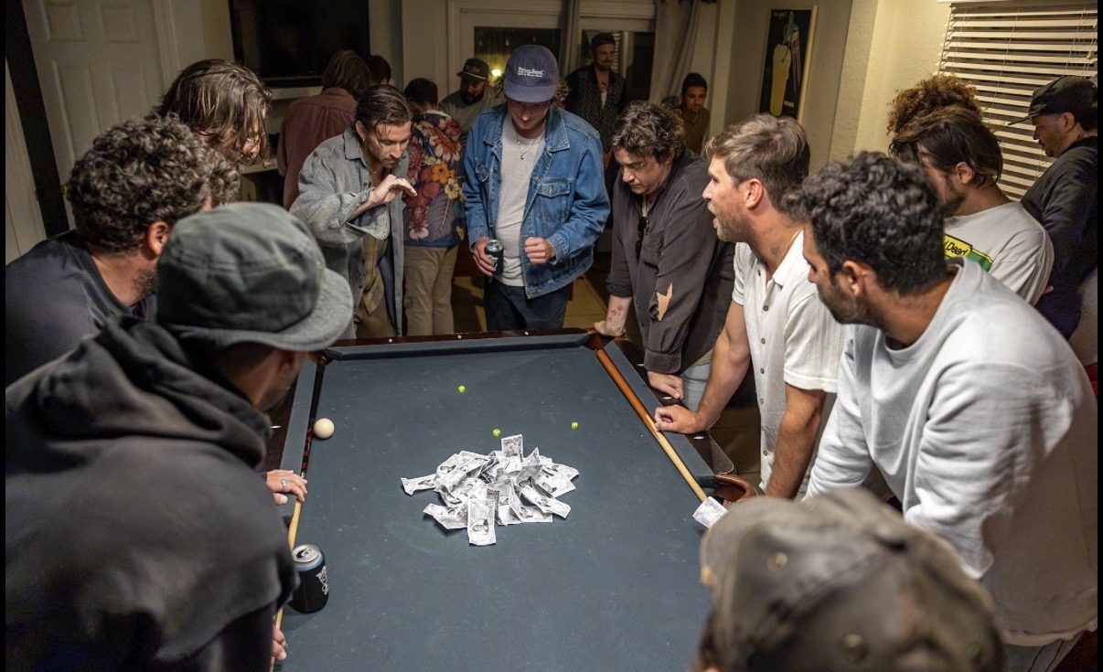 Men gathered around a pool table converted into a dice table, with the remaining money supply piled at the center.