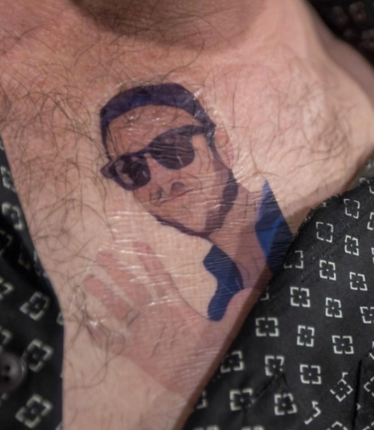 A close-up of a temporary tattoo of a suited man in sunglasses applied to someone's neck.