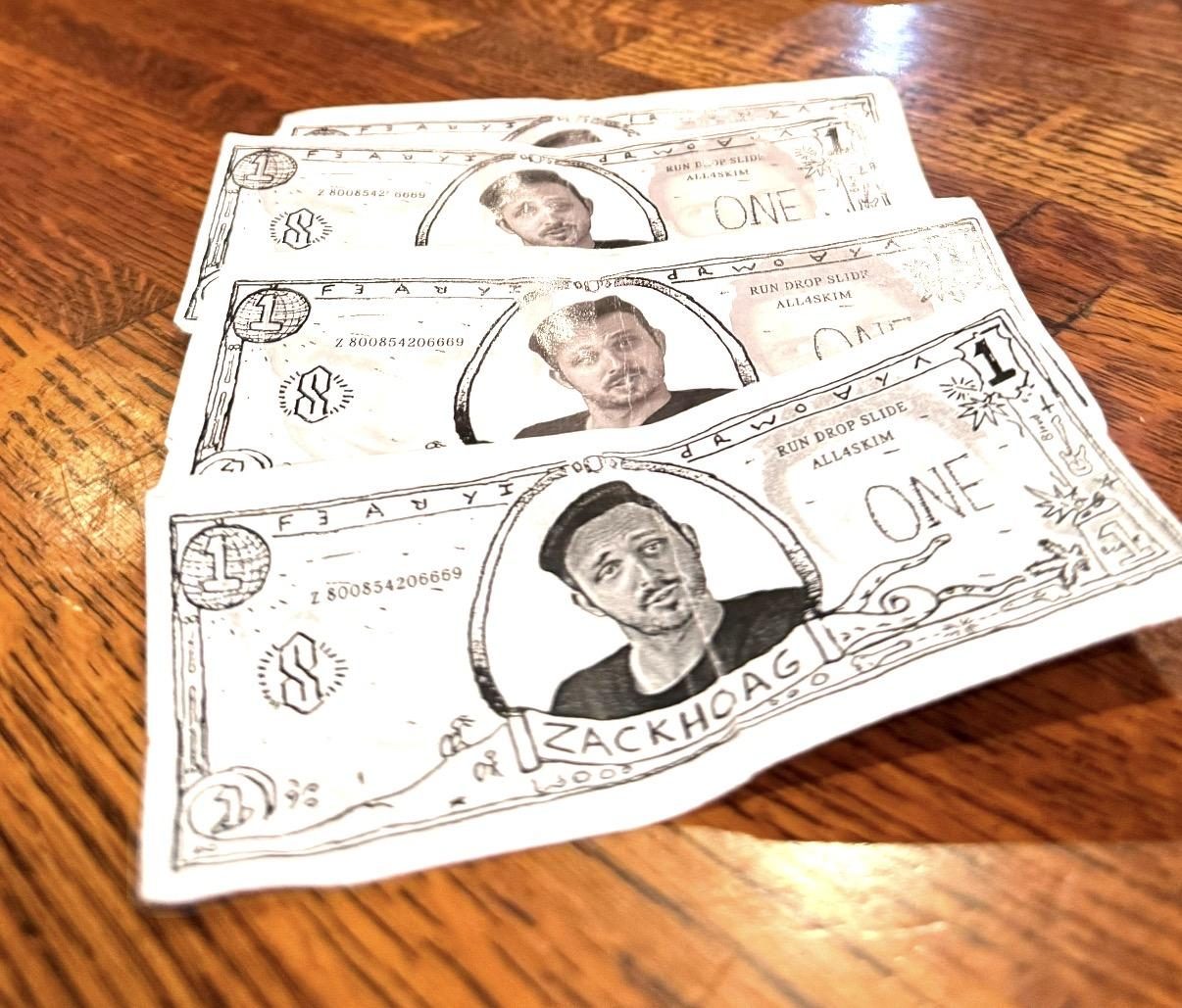 Three one-unit Zack Back notes fanned out on a wooden table.