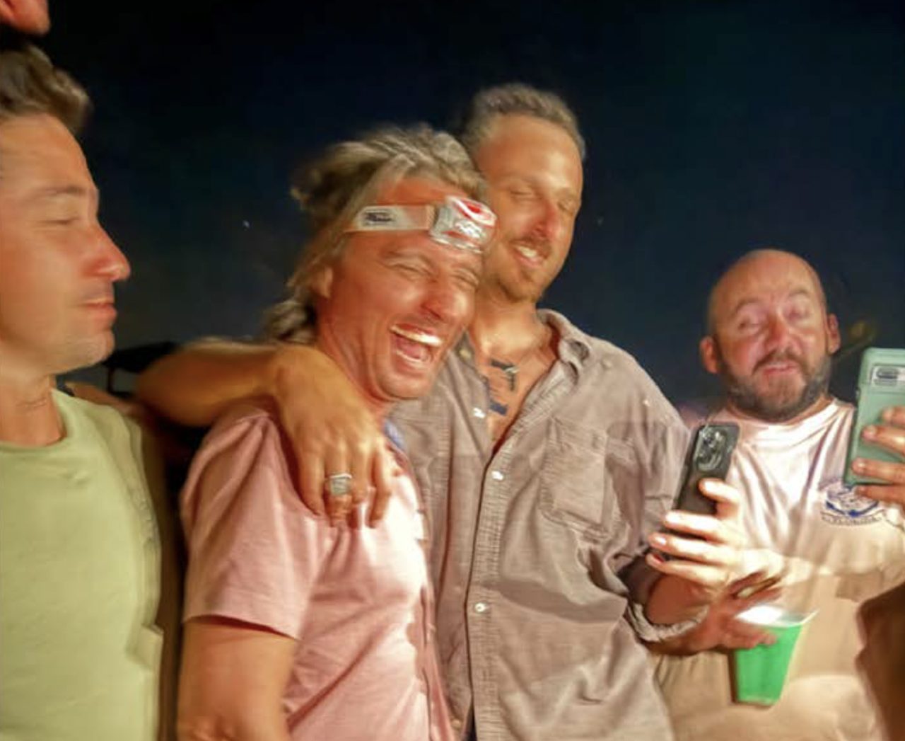 Four men howling and staggering along the shoreline at dusk.