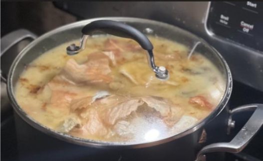 A large covered pot of simmering broth and meat on a stovetop.